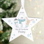 Star-shaped Christmas ornament with cartoon characters and text, hanging against a blurred Christmas tree background.