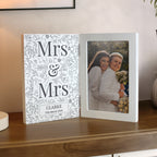 Personalized photo album with 'Mrs & Mrs' design on a wooden surface.