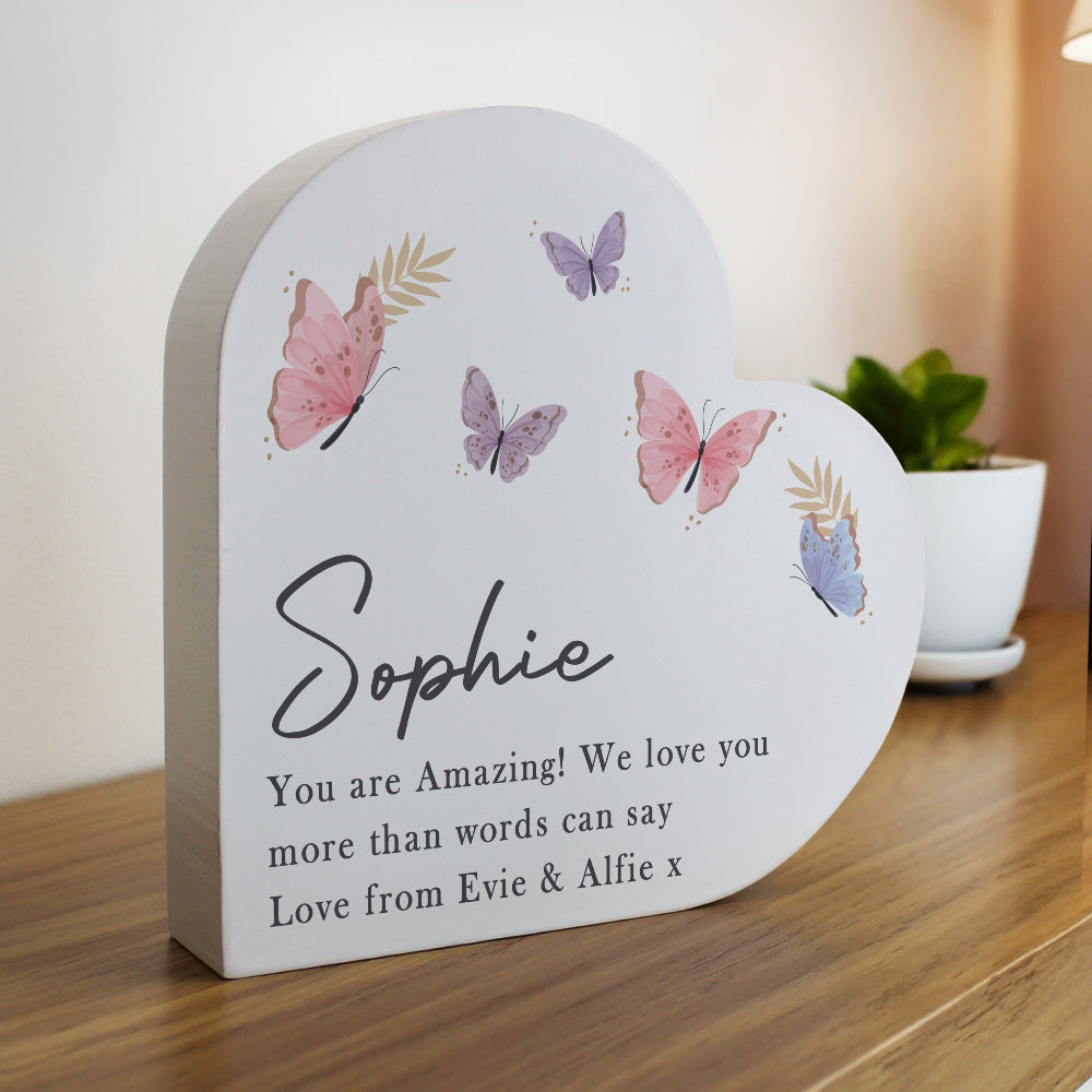 Heart-shaped wooden plaque with butterflies and personalized message on a wooden surface.