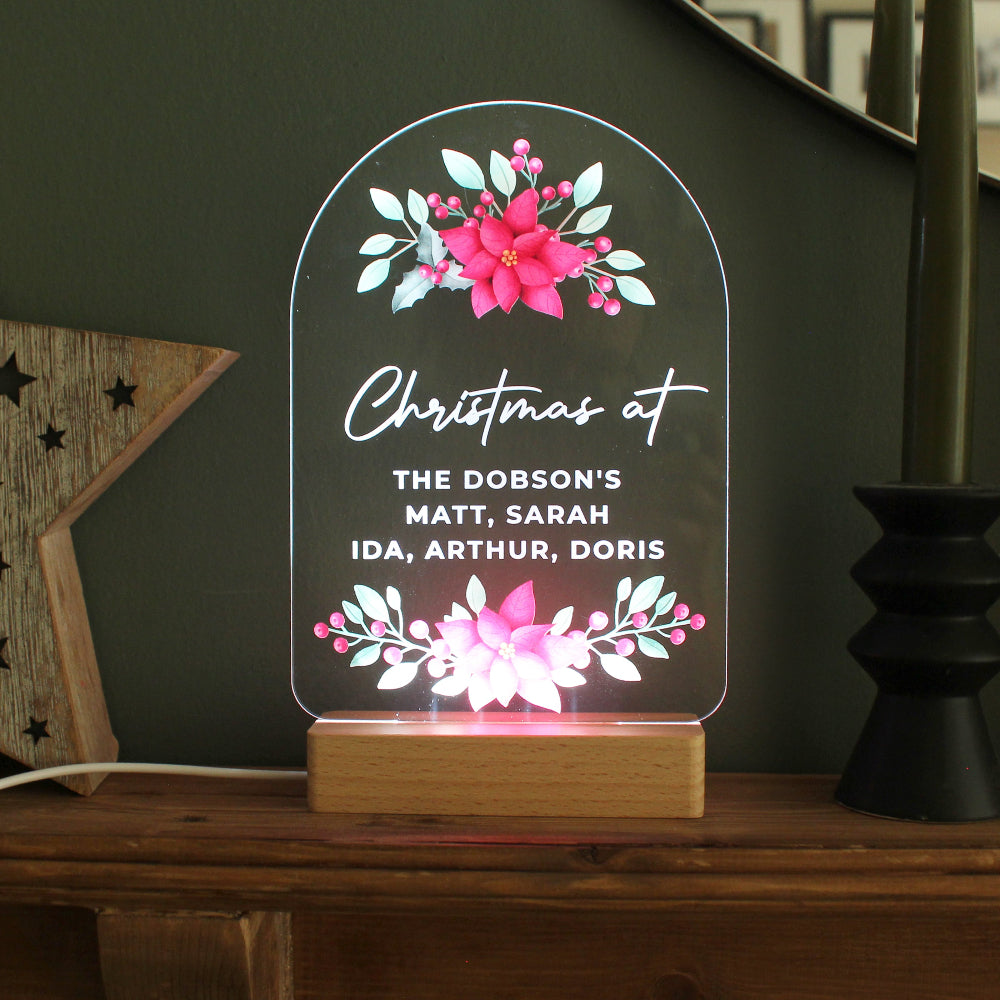 Decorative LED sign with floral design and text on a wooden base, placed on a dark surface.