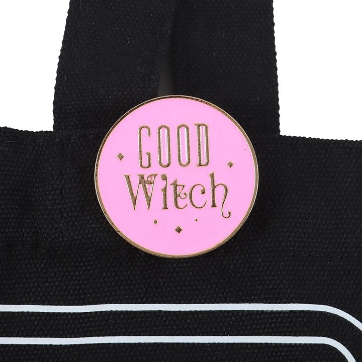 Pink 'Good Witch' enamel pin on a black bag with white stripes