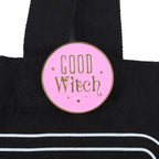 Pink 'Good Witch' enamel pin on a black bag with white stripes