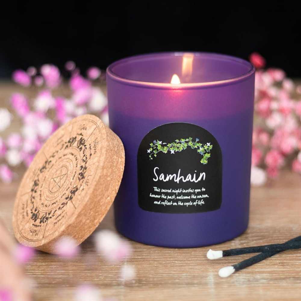 Purple candle with a 'Samhain' label on a wooden surface with blurred flowers in the background