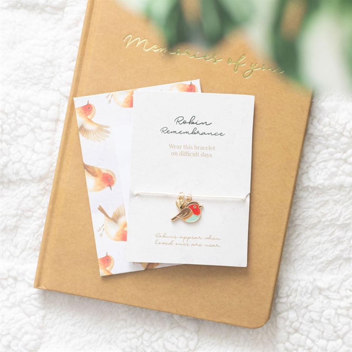 Bird-shaped earring on a card with 'Memories of You' text, placed on a textured surface.