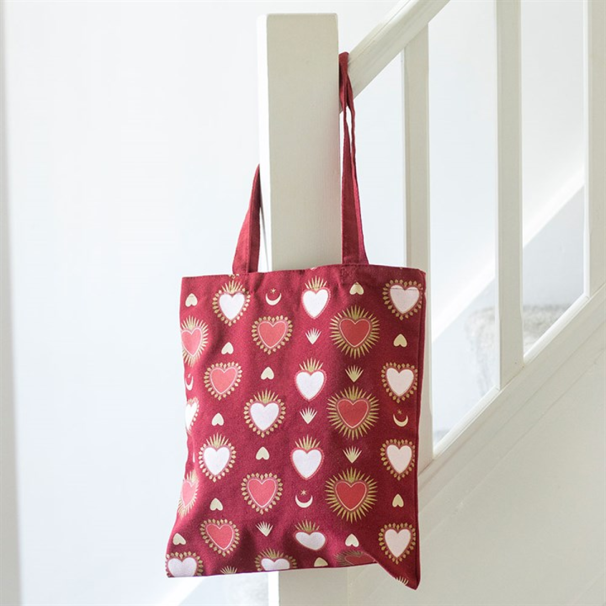 Red tote bag with heart pattern hanging on a white railing.