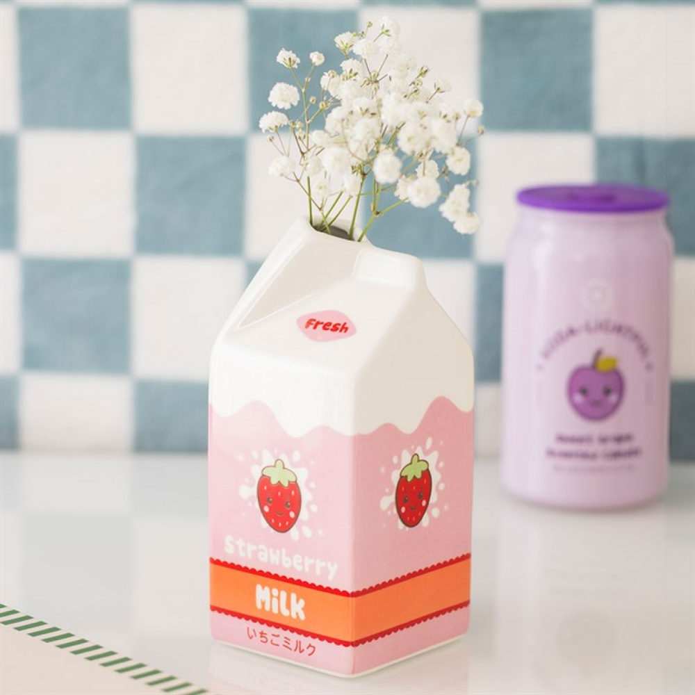 Carton of strawberry milk with a small vase of white flowers on a checkered background