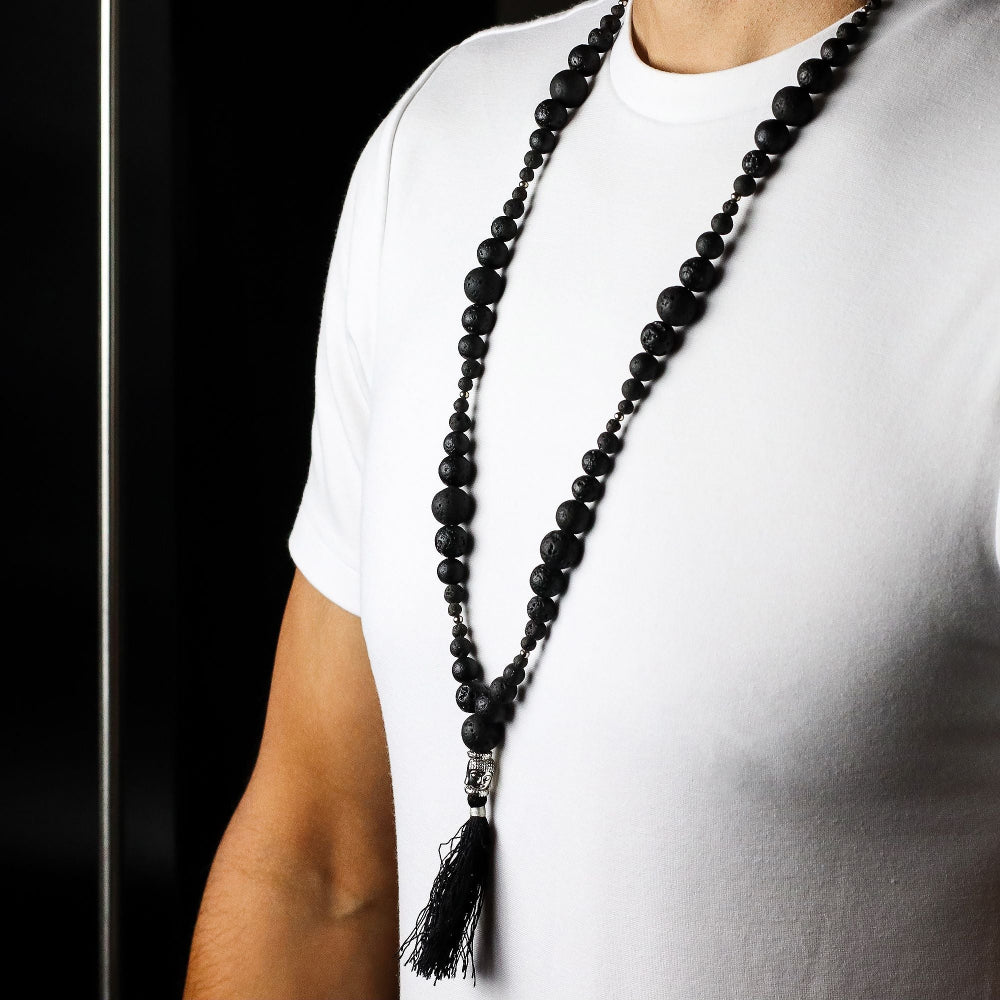 Person wearing a long black beaded necklace with a tassel on a white background