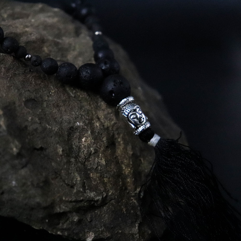 Black beaded necklace with a silver tassel on a stone surface