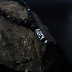Black beaded necklace with a silver tassel on a stone surface