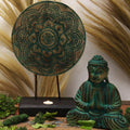 Decorative setup with a mandala, Buddha statue, and candles on a wooden surface.