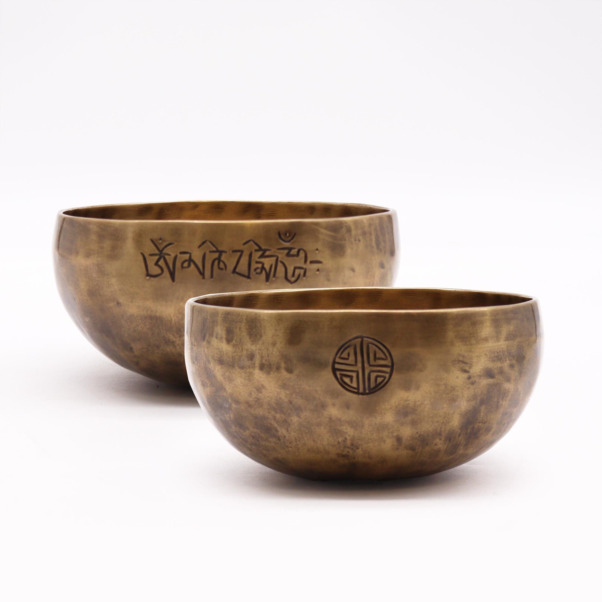Two bronze singing bowls with engraved symbols on a white background