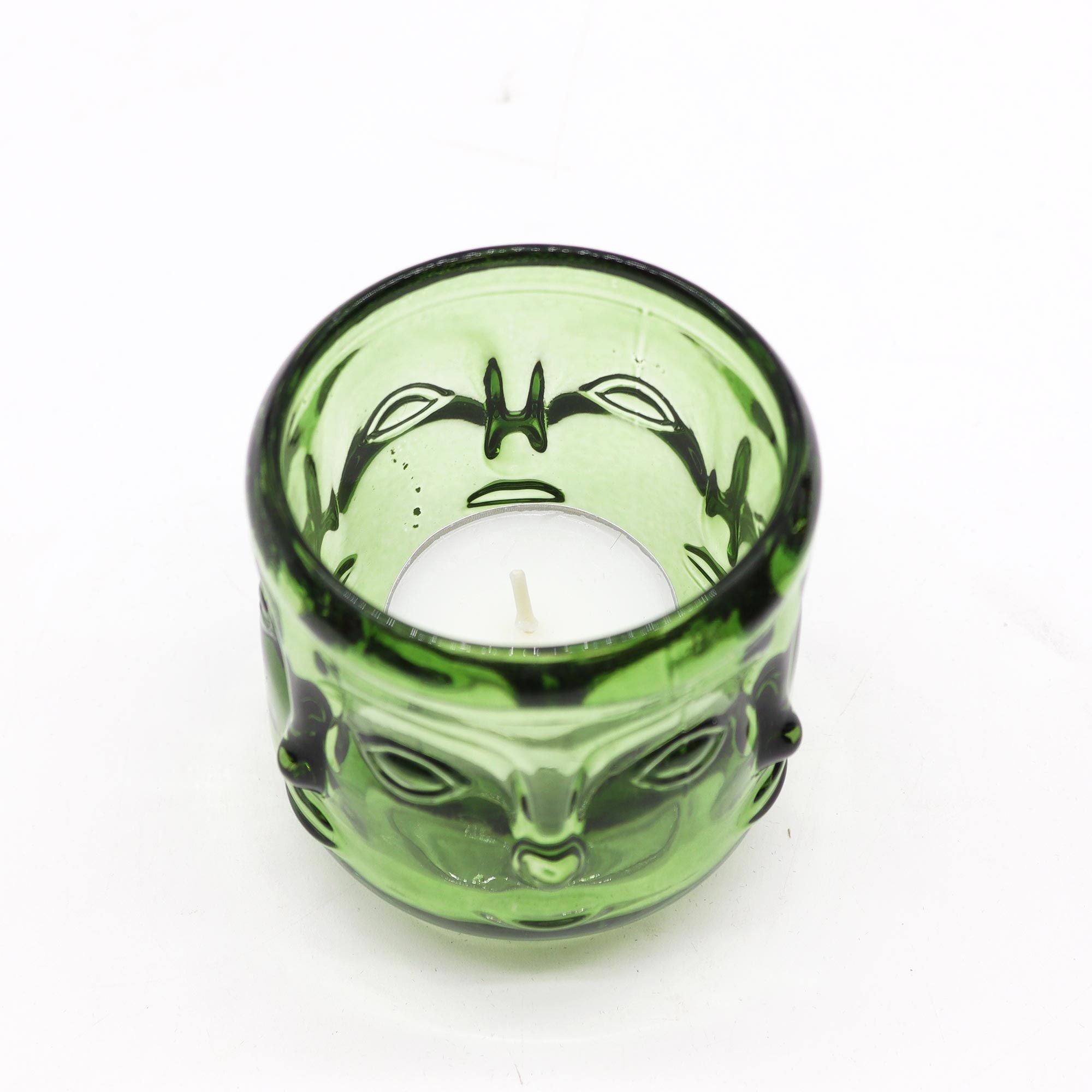 Green glass candle holder with alien face design on a white background