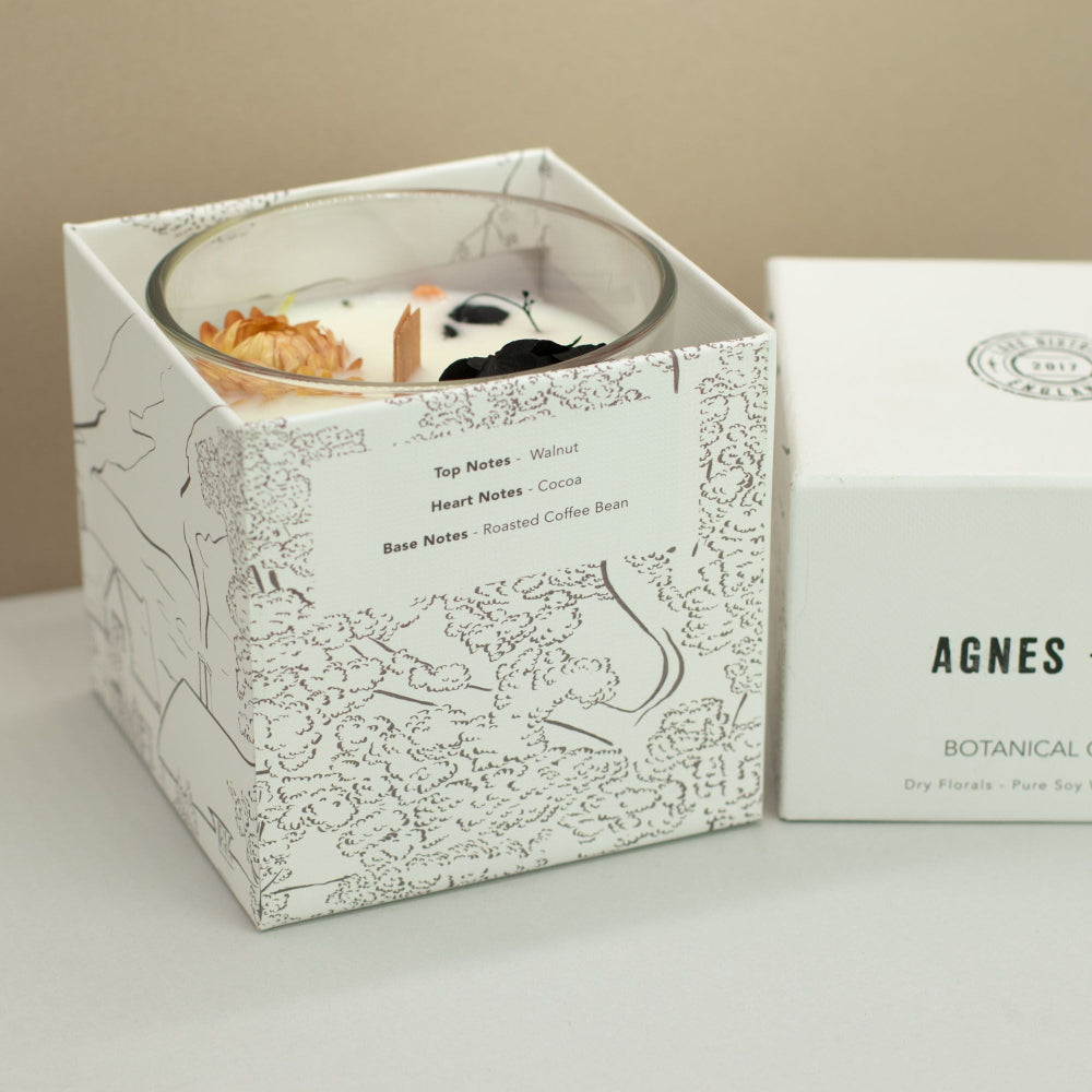 Candle in a decorative box with botanical design, next to a box labeled 'AGNES'.