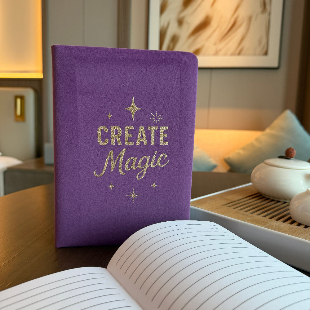 Purple notebook with 'Create Magic' text on a wooden table in a cozy room.