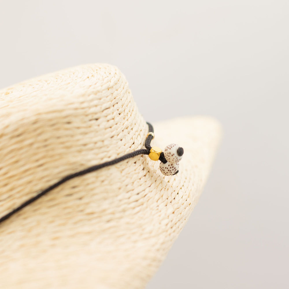 Straw hat with a decorative band featuring a small animal figure on a light gray background