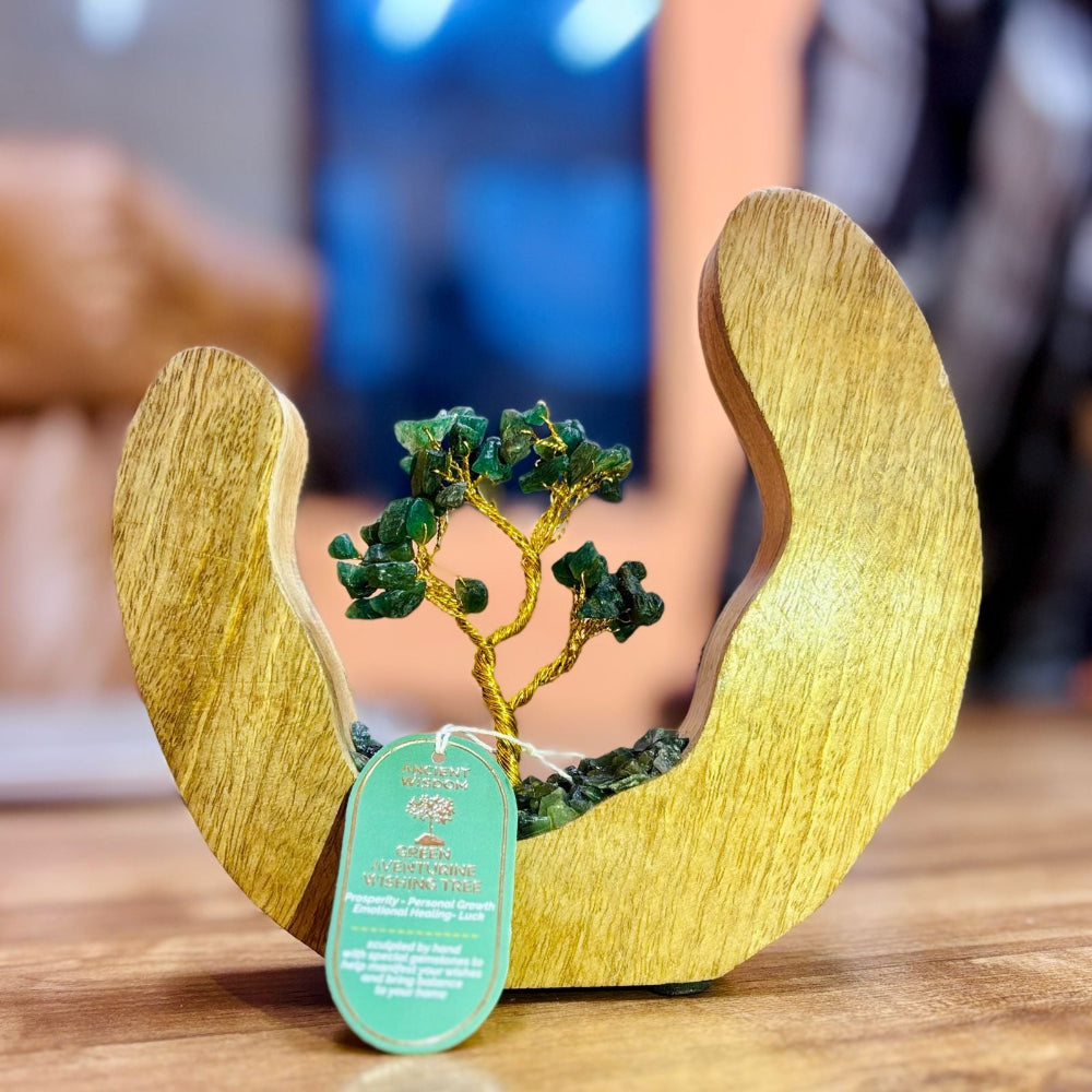 Decorative item with a gold tree and green stones inside wooden wings on a table.
