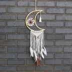 Decorative dreamcatcher with feathers hanging against a brick wall.