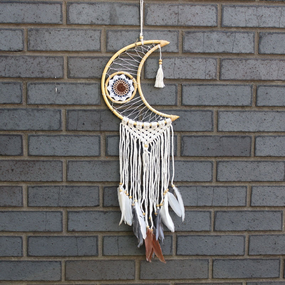 Decorative dreamcatcher with feathers hanging against a brick wall.