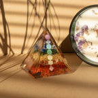 Pyramid-shaped crystal with colorful stones and a candle with flowers on a beige surface