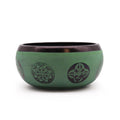 Green singing bowl with purple designs on a white background