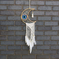 Decorative dreamcatcher with feathers hanging against a brick wall.
