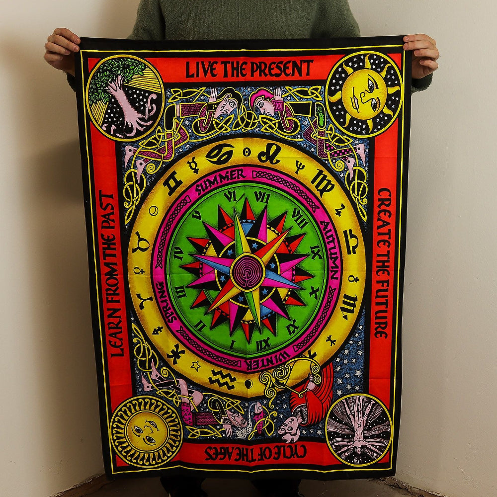 Person holding a colorful tapestry with symbols and text against a plain wall.