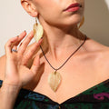 Woman wearing gold leaf earrings and necklace against a neutral background