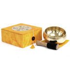 Gold singing bowl set with wooden striker and yellow box on a white background