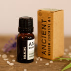 Bottle and box of essential oil on a wooden surface with flowers in the background