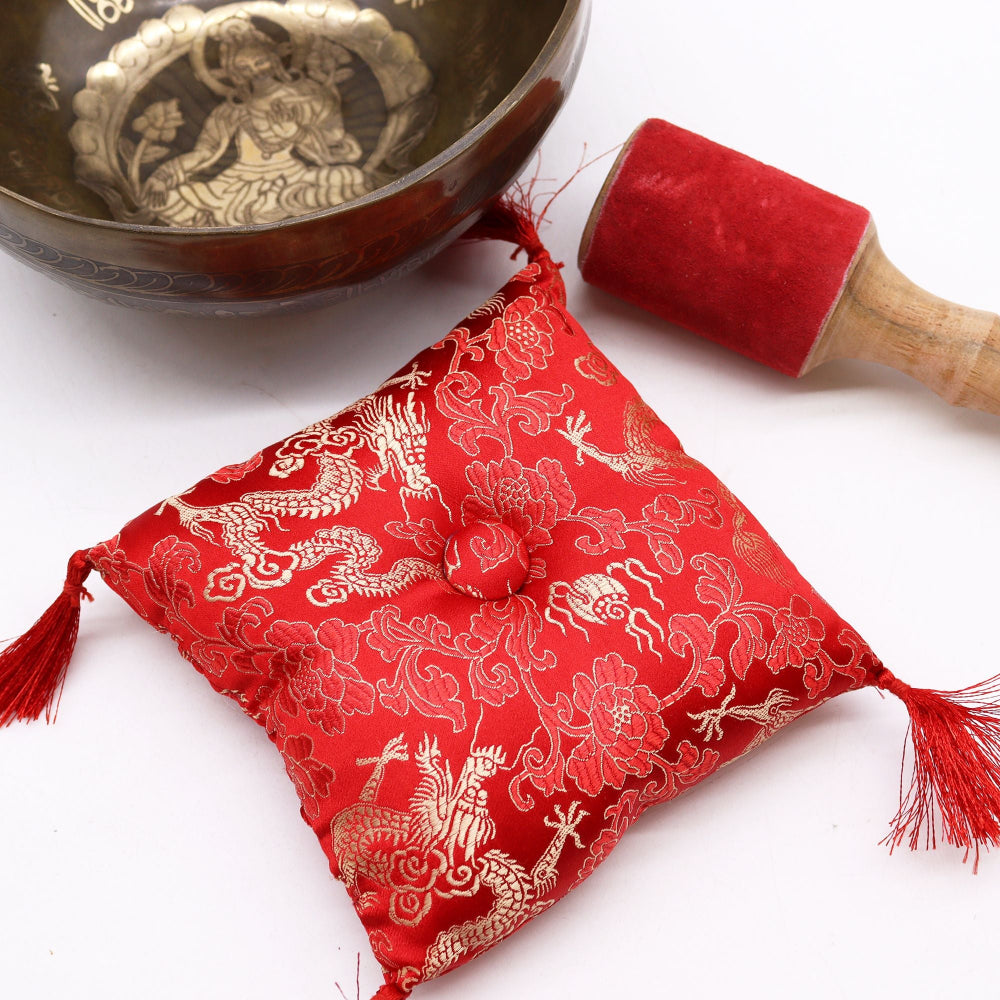 Red fabric pouch with gold designs, a wooden mallet, and a metal singing bowl on a white background