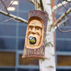 Wooden birdhouse with a face design and a blue tit bird perched on it, hanging from a tree.