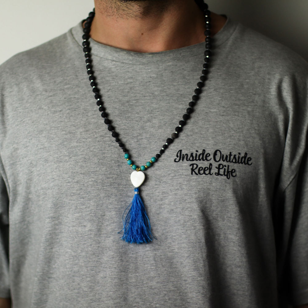 Person wearing a gray t-shirt with text and a beaded necklace with a blue tassel.