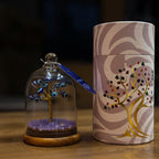 Decorative item with a tree inside a glass dome and a matching cylindrical container on a wooden surface.