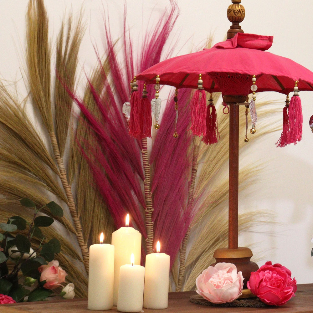 Decorative pink umbrella with tassels, candles, and flowers on a table.