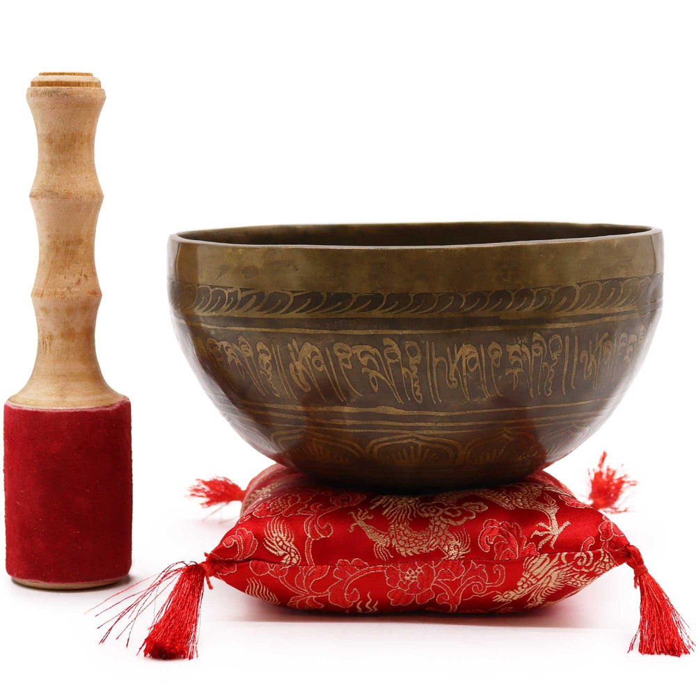 Tibetan singing bowl with wooden striker and red cushion on a white background