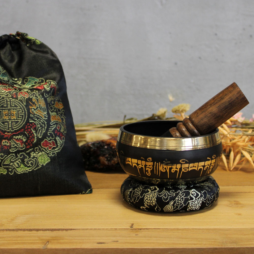 Tibetan singing bowl with wooden striker on a wooden surface, with a decorative bag in the background.