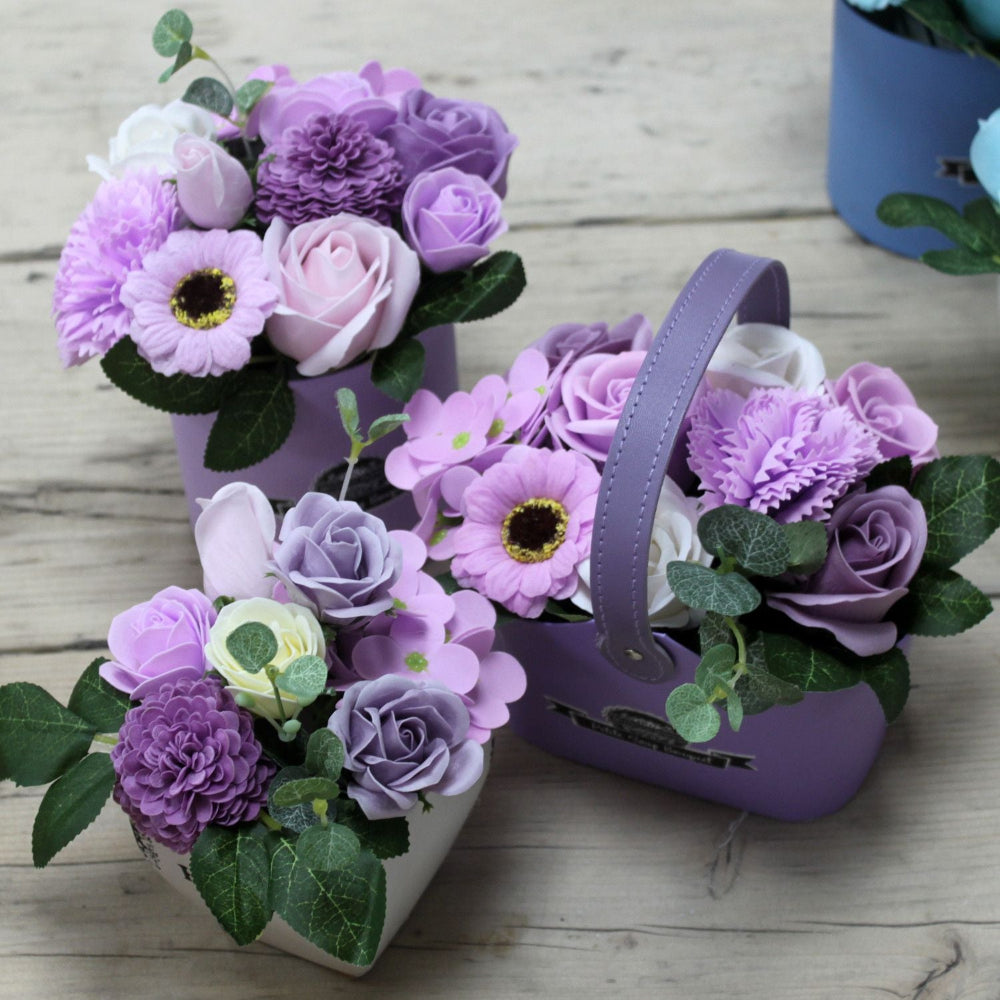 Three purple flower arrangements in decorative containers on a wooden surface