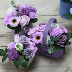 Three purple flower arrangements in decorative containers on a wooden surface