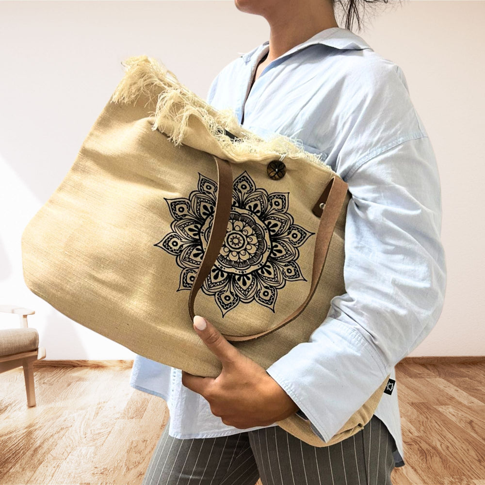 Person holding a beige tote bag with a black mandala design.