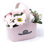 Pink floral arrangement in a decorative basket with 'Petite Soie Boutique' label on a white background
