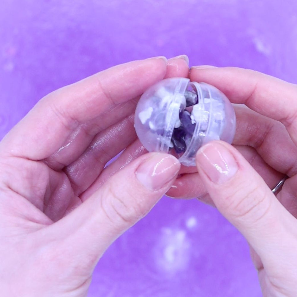 Clear plastic ball with puzzle pieces inside, held between two hands against a purple background
