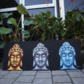 Canvas print with three Buddha faces in gold, silver, and blue on a black background, placed outdoors.