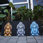 Canvas print with three Buddha faces in gold, silver, and blue on a black background, placed outdoors.