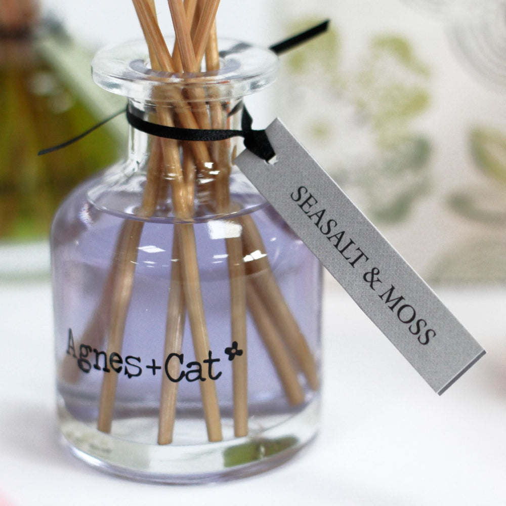 Glass diffuser bottle with wooden sticks and a label reading 'Seasalt & Moss' by 'Agnes + Cat'.