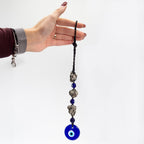 Hand holding a necklace with blue evil eye bead against a white background