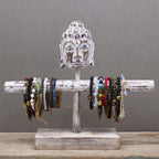 Wooden bracelet holder with Buddha head design displaying various bracelets on a gray background