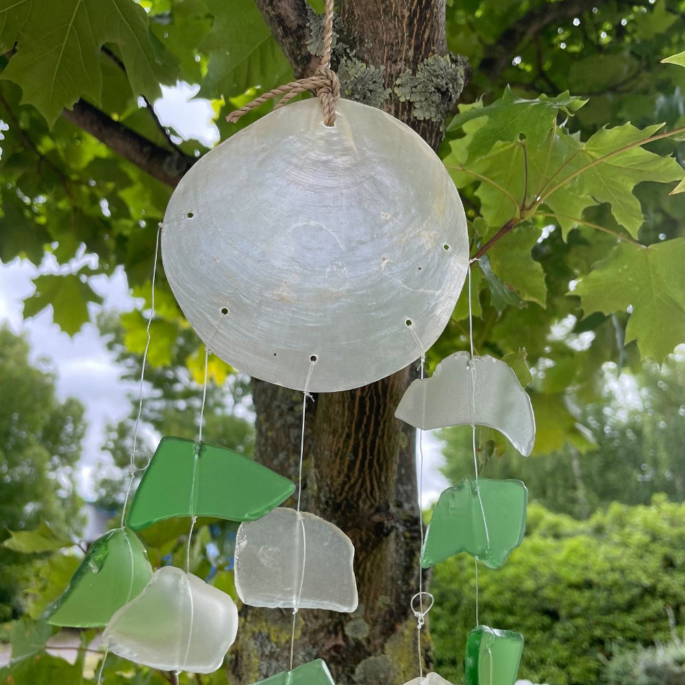 Decorative hanging shell with green and clear pieces against a tree background