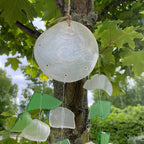 Decorative hanging shell with green and clear pieces against a tree background