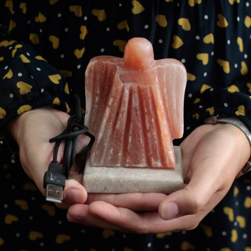 Himalayan salt lamp shaped like an angel held in hands with a USB cable.