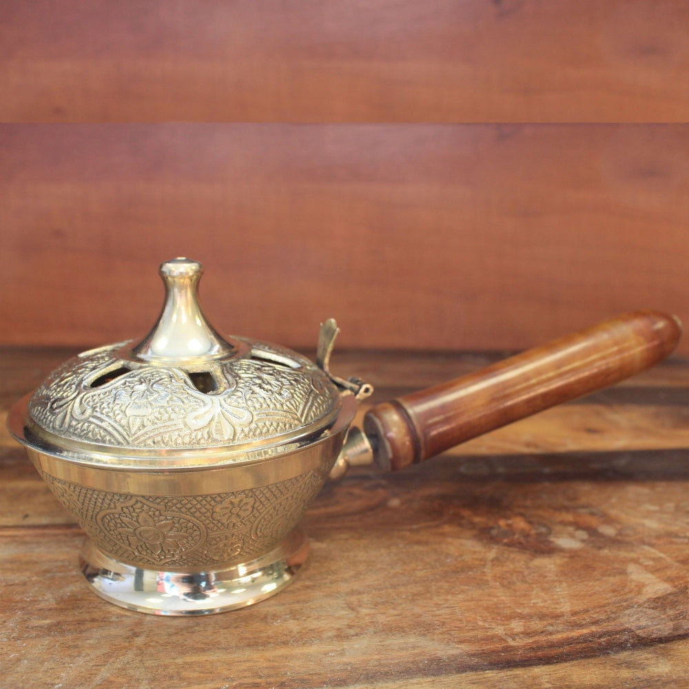 Brass incense burner with wooden handle on a wooden surface